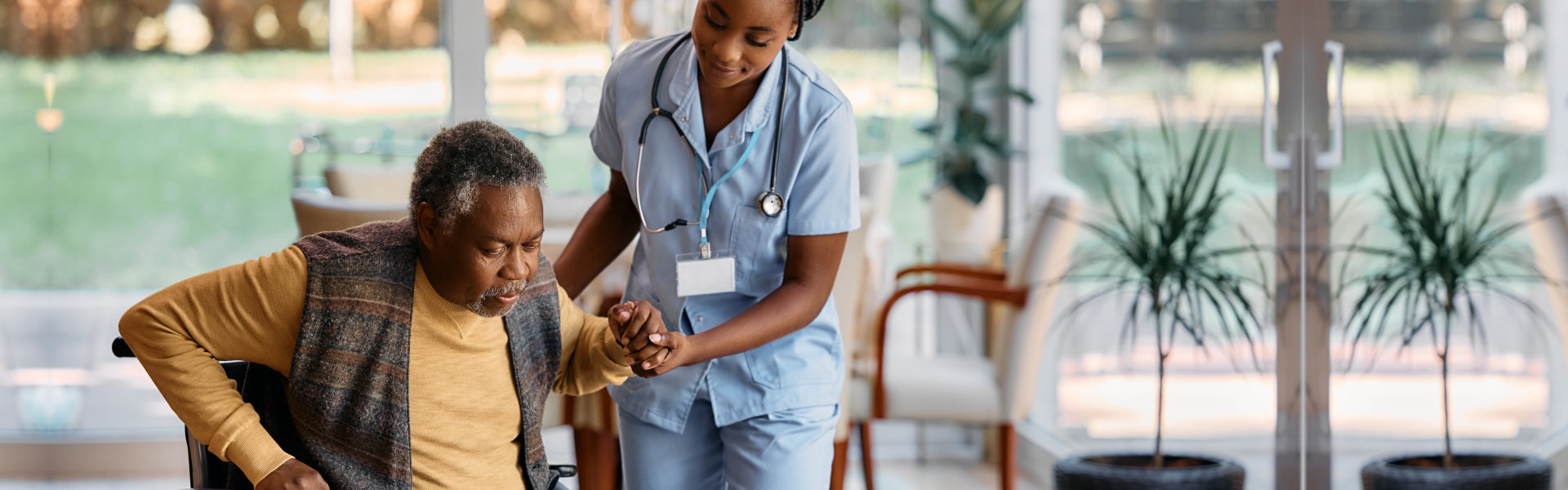 Nurse assists male elderly patient to stand from wheelchair